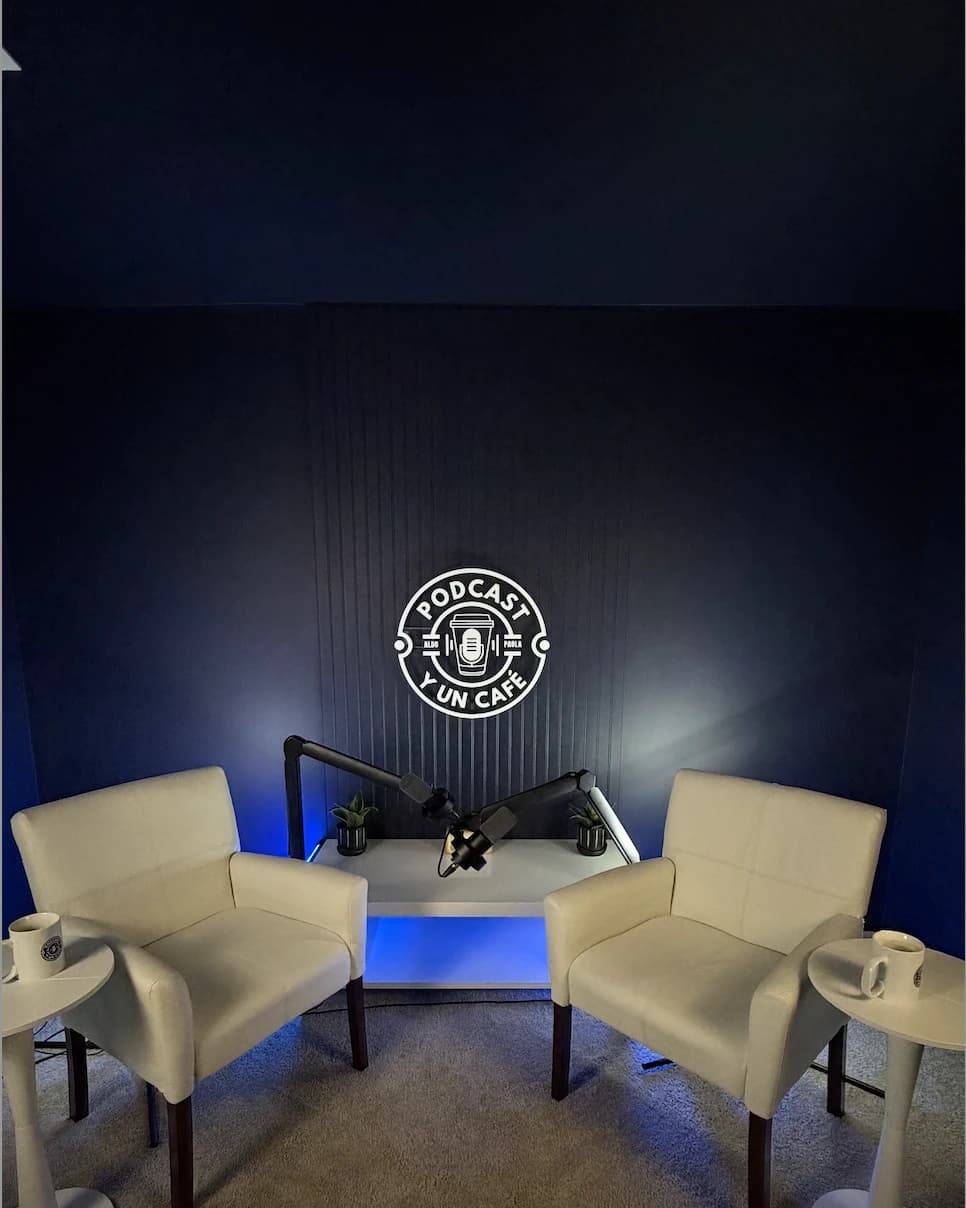 El set de Podcast y un Café vacío: dos sillones, dos tazas servidas y el logo en neón sobre la pared