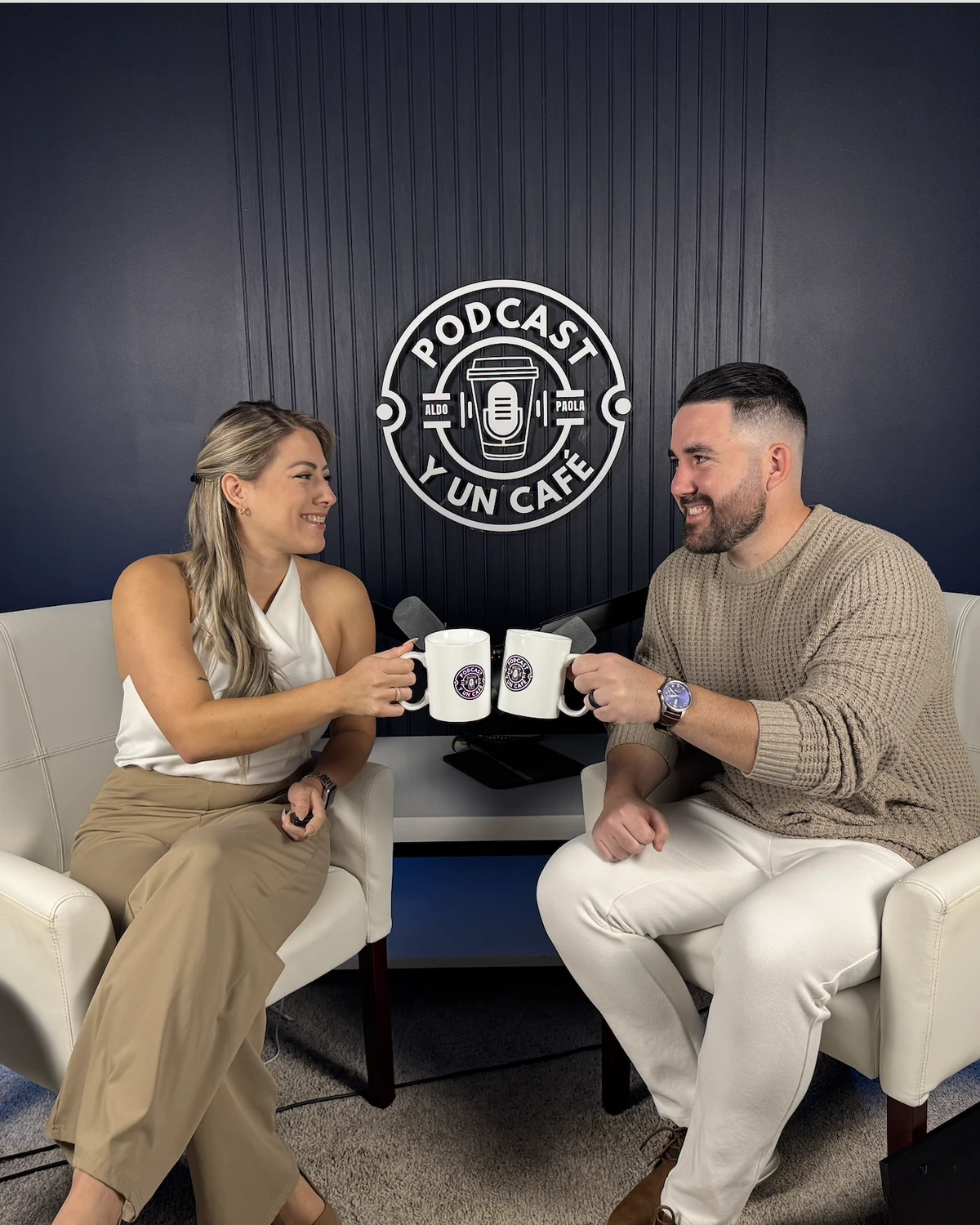 Aldo Ramírez y Paola Asaro brindando con dos tazas bajo el logo de Podcast y un Café
